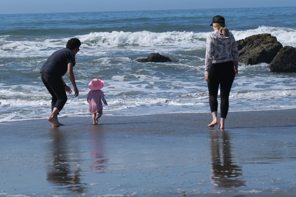 Parents follow a very young girl as she runs towards the crashing waves. Dad is poised to grab her if necessary.