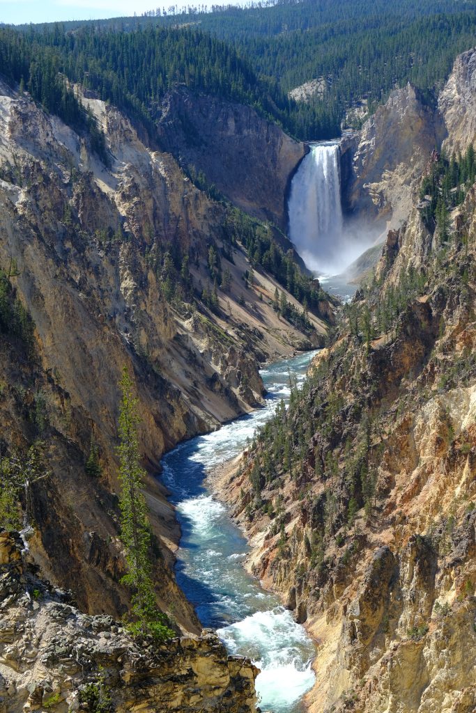 From top to bottom: A hint of blue sky, evergreen forest, large waterfall, steep rocky canyon walls on both sides.  The river, punctuated by rapids, roars to the bottom of our view.